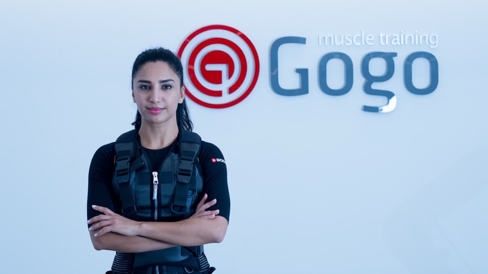 A client in an EMS suit standing confidently in front of the GoGo logo